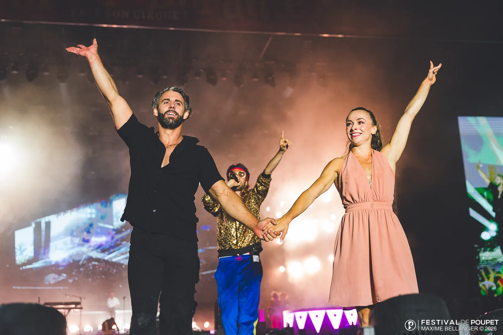 Des artistes saluent le public sur la grande scène du Festival de Poupet, bras levés