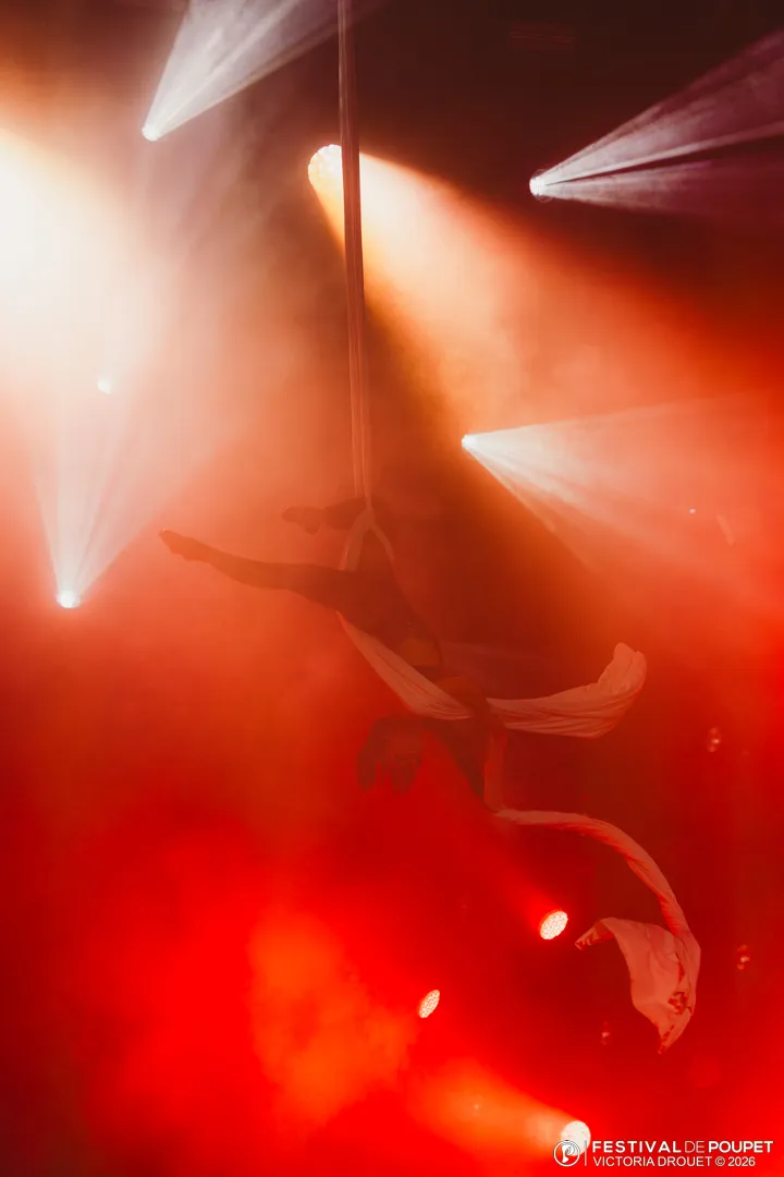 Une artiste aérienne en suspension dans les faisceaux de lumière rouge
