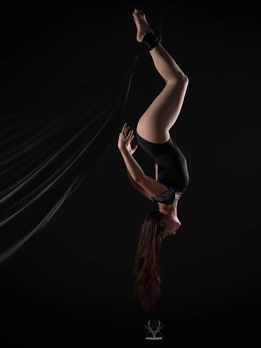 Une artiste la tête en bas, accrochée à un tissu aérien sur fond noir